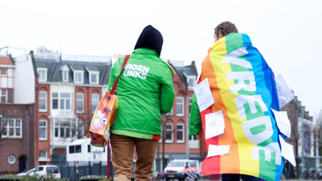 Twee GroenLinks mensen, een met een Pride vlag waarom VREDE staat